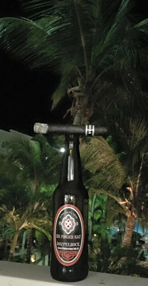 A bottle of Six Finger Kat outdoors under palm trees