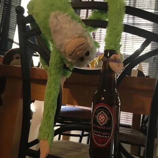 A bottle of Six Finger Kat on a table next to a plush toy monkey