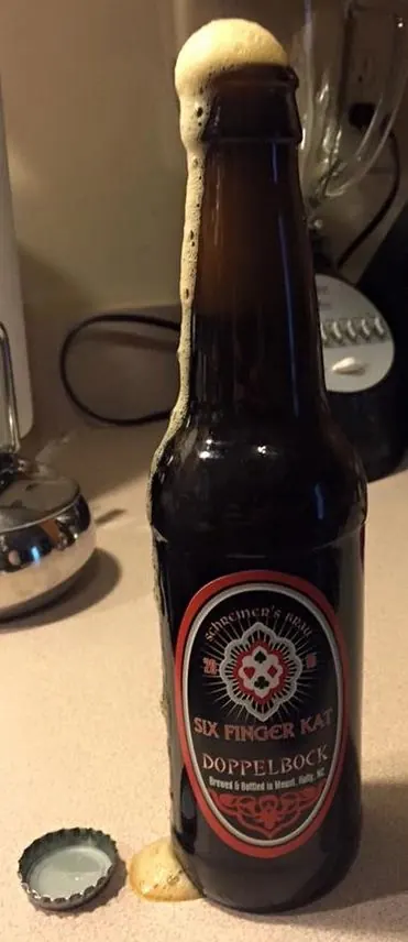 A freshly opened bottle of Six Finger Kat Doppelbock foaming over onto the counter