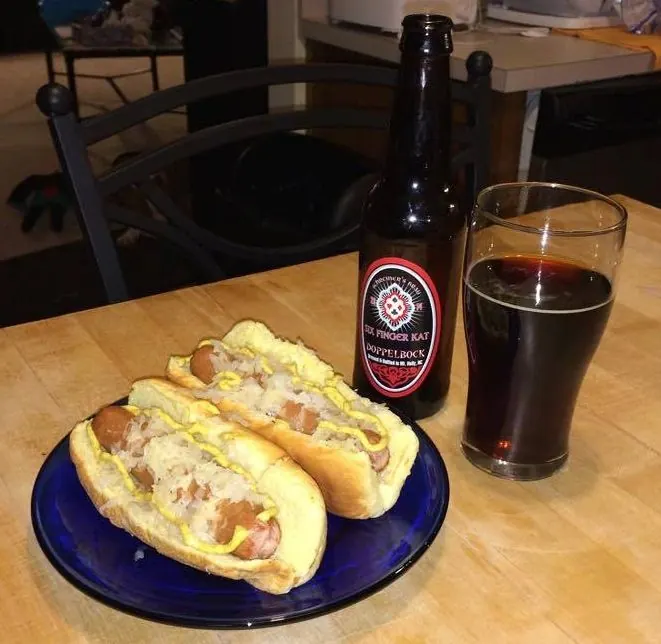 A bottle and a glass of Six Finger Kat beside sausages in buns